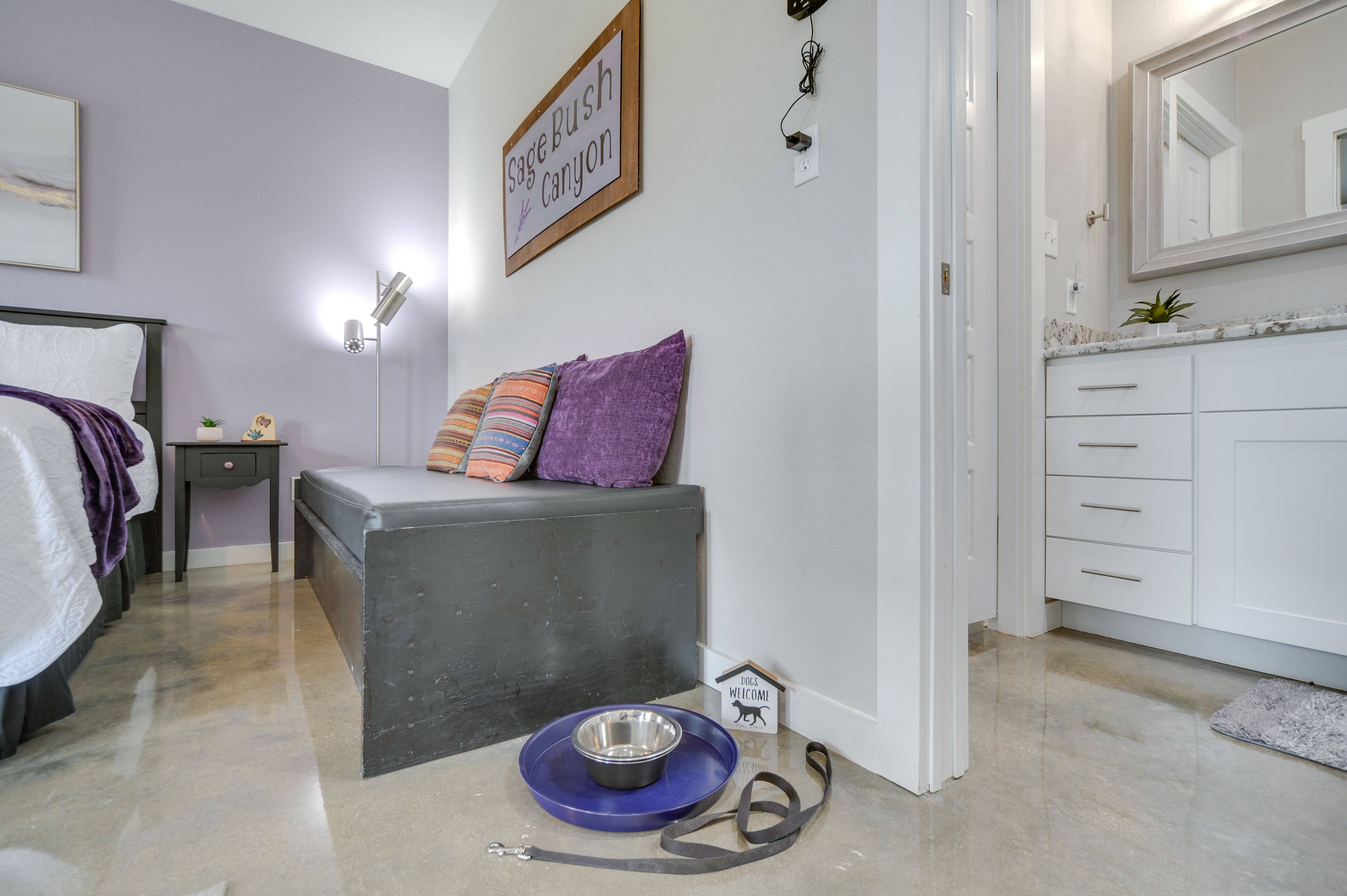 A bedroom with a bed, bedside table, lamp, and a wall sign reading "Sage Bush Canyon".