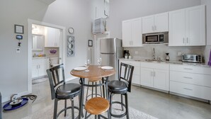 A modern kitchen with white cabinets, a stainless steel refrigerator, and a microwave. There is a dining table with four chairs and a small rug on the floor.