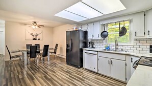A modern kitchen with a large refrigerator, white cabinets, a dining area with a glass table and chairs, and a skylight above.