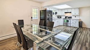 A modern kitchen with white cabinets, a black refrigerator, and a dining area with a glass table and chairs.