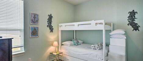 A bunk bed in a room with light green walls, a small bedside table with a lamp, and decorative wall art.
