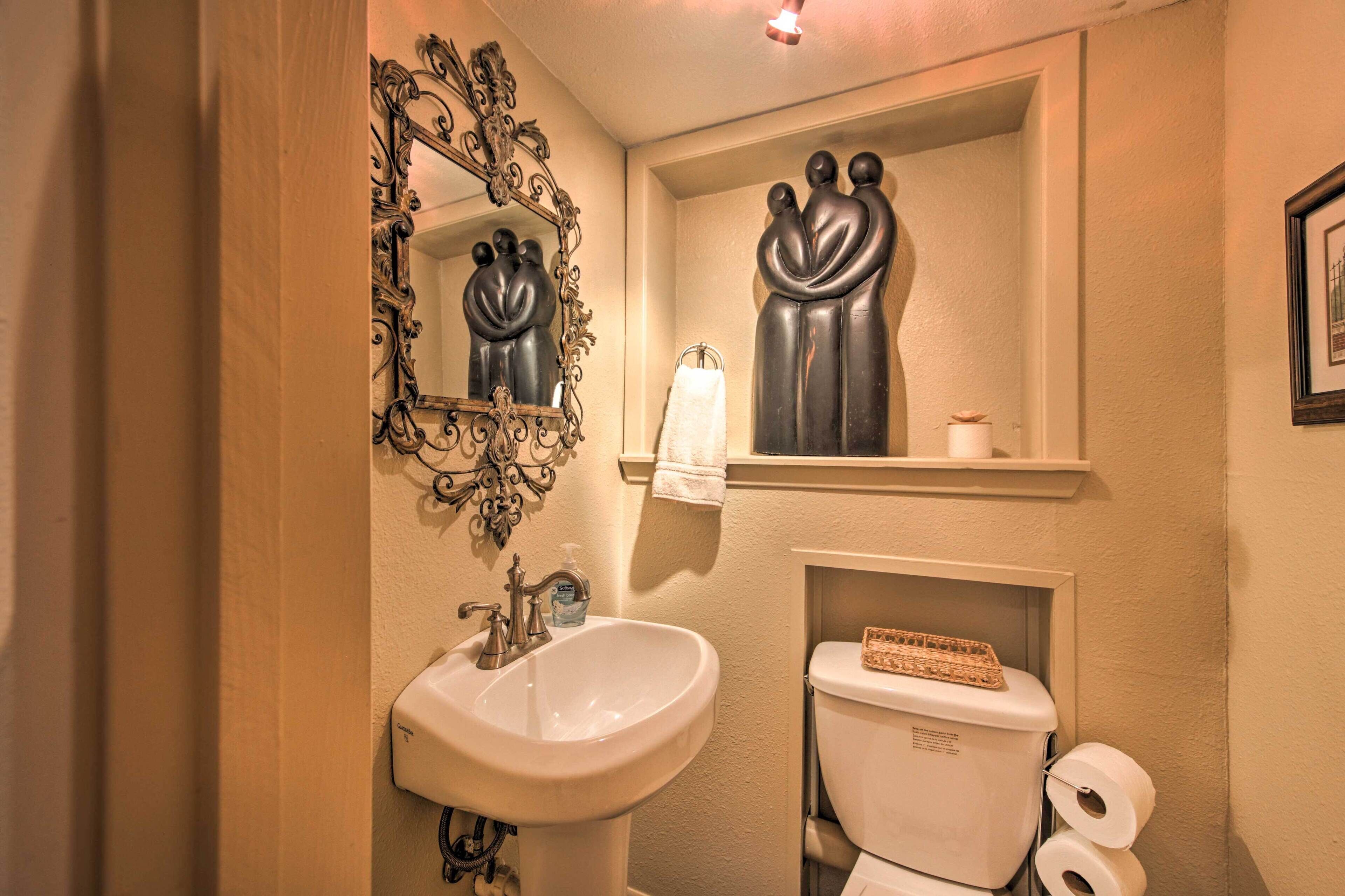 A bathroom with a white sink, ornate mirror, and a toilet with a shelf above it.