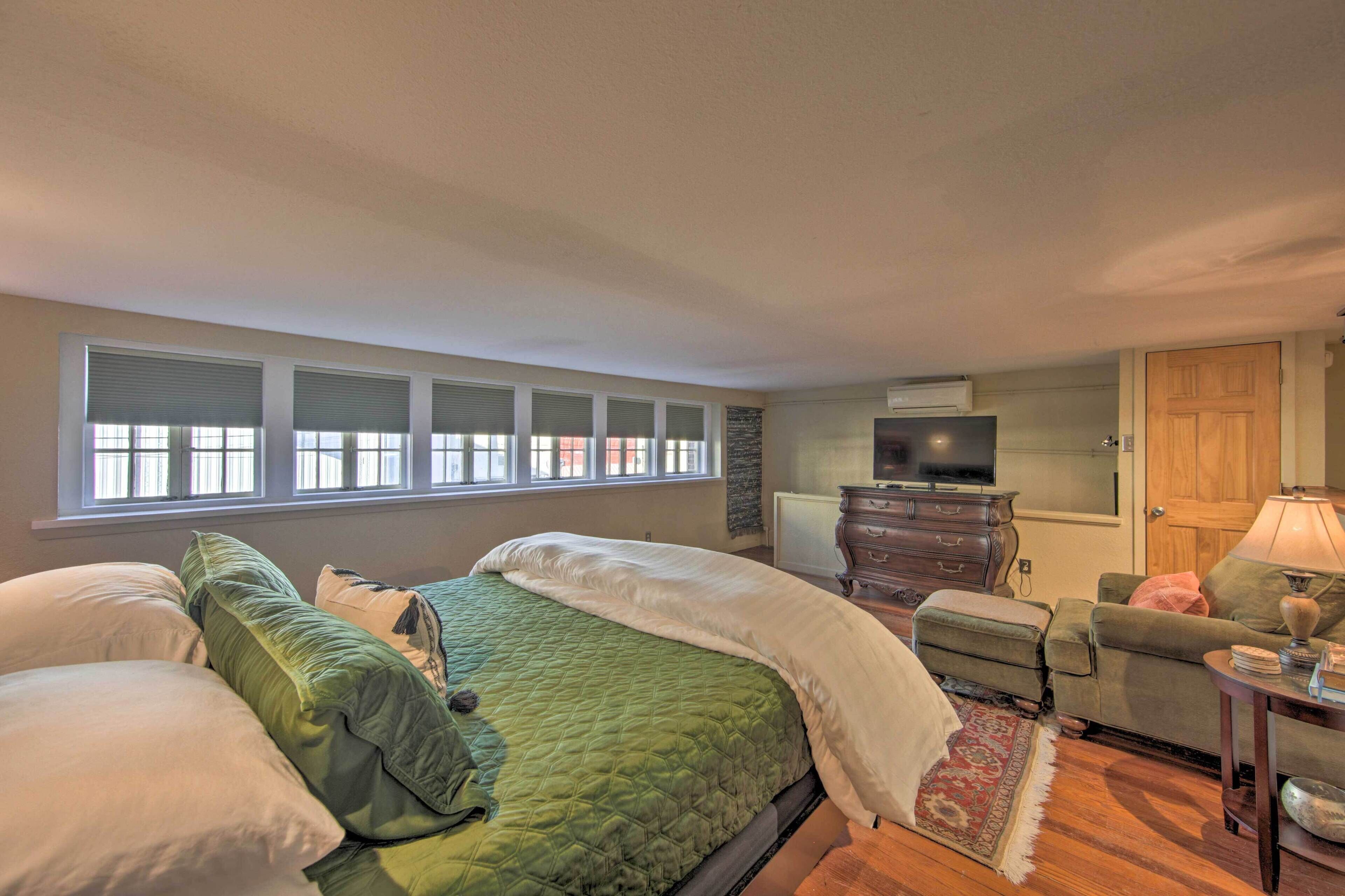 A bedroom with a large bed, a dresser, a television, and a window with blinds.