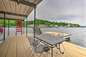 A wooden deck with a table and chairs, overlooking a lake with houses in the background. - 2 Decks, Dock, Fire Pit! Waterfront Lake Ozark Gem (Lake Ozark)