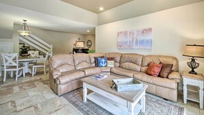 A living room with a beige sectional sofa, a coffee table, and a dining area with a white table and chairs.