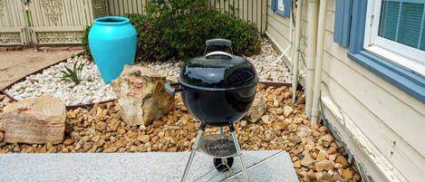 A barbecue grill on a concrete patio with a decorative blue vase and a wooden fence in the background.