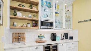 A modern kitchen with white cabinets, a built-in microwave, a coffee maker, and a toaster. - Magnolia Cottage by Miss Kitty’s (Rockport)