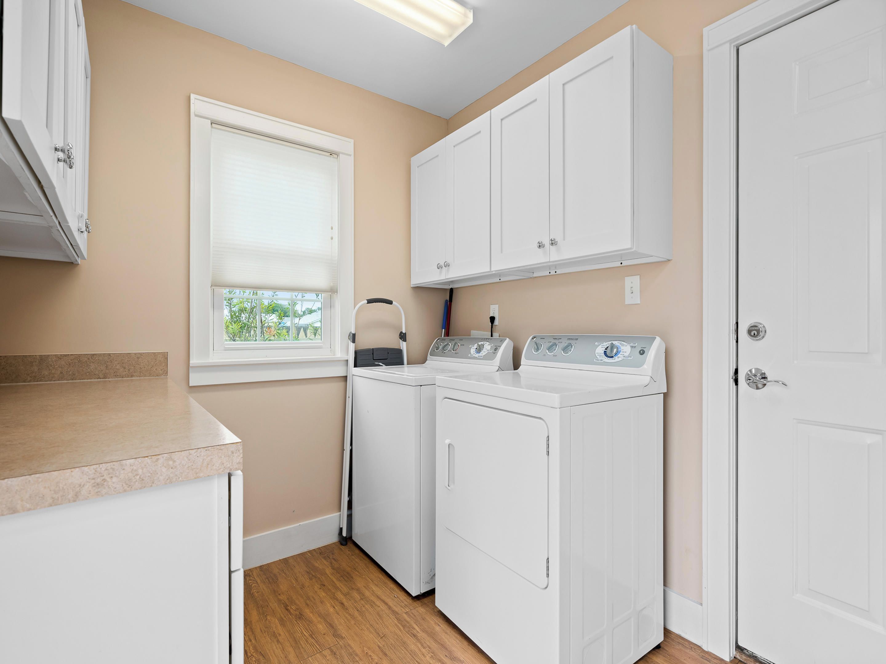 A laundry room with two white washing machines, a window with blinds, and a door.