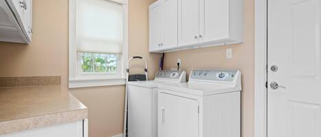 A laundry room with two white washing machines, a window with blinds, and a door.