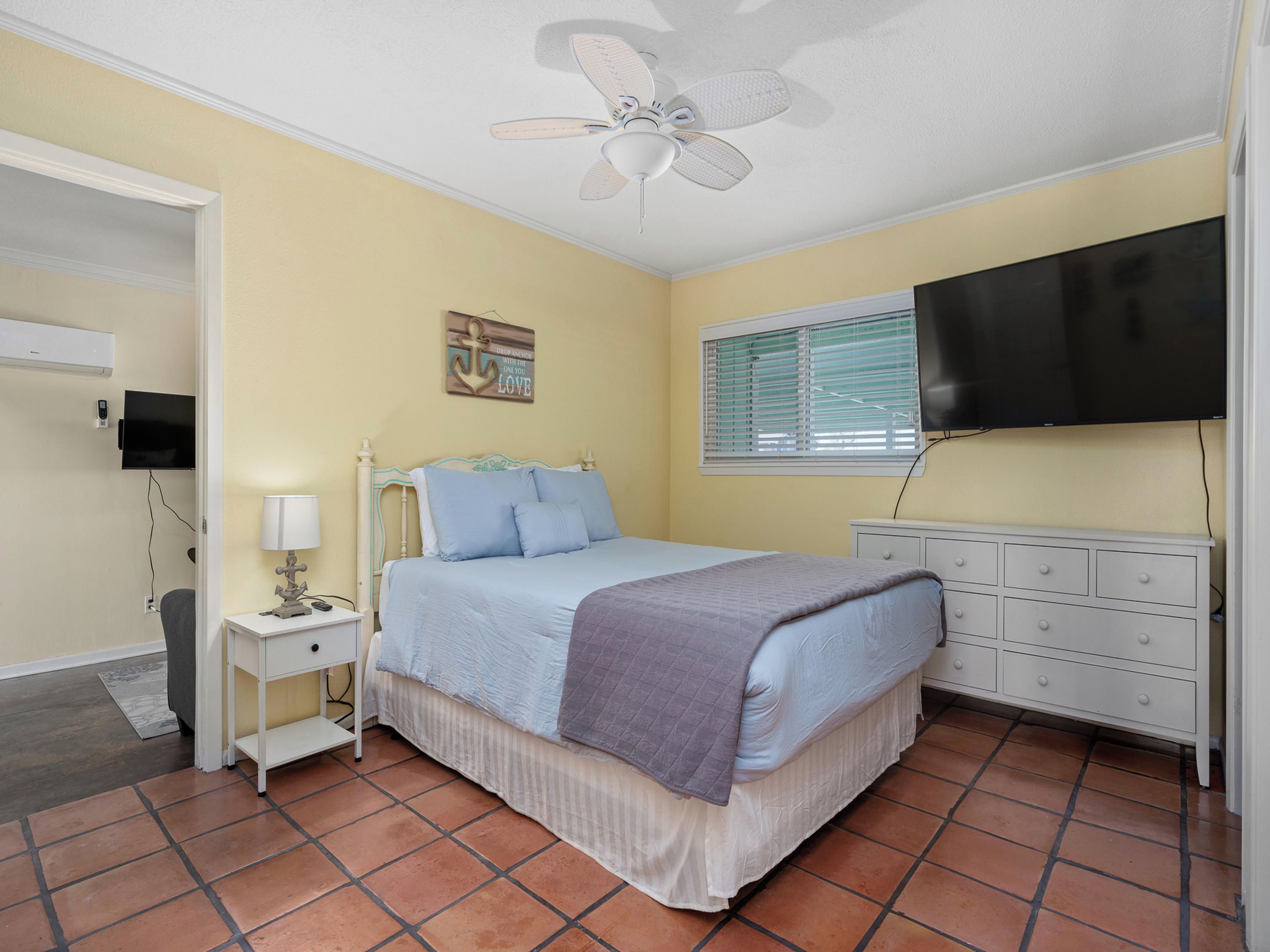 Une chambre à coucher comprenant un lit, une table de chevet, une commode, un téléviseur et un ventilateur de plafond.