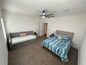 A bedroom with a bed, a sofa, a ceiling fan, and a door.