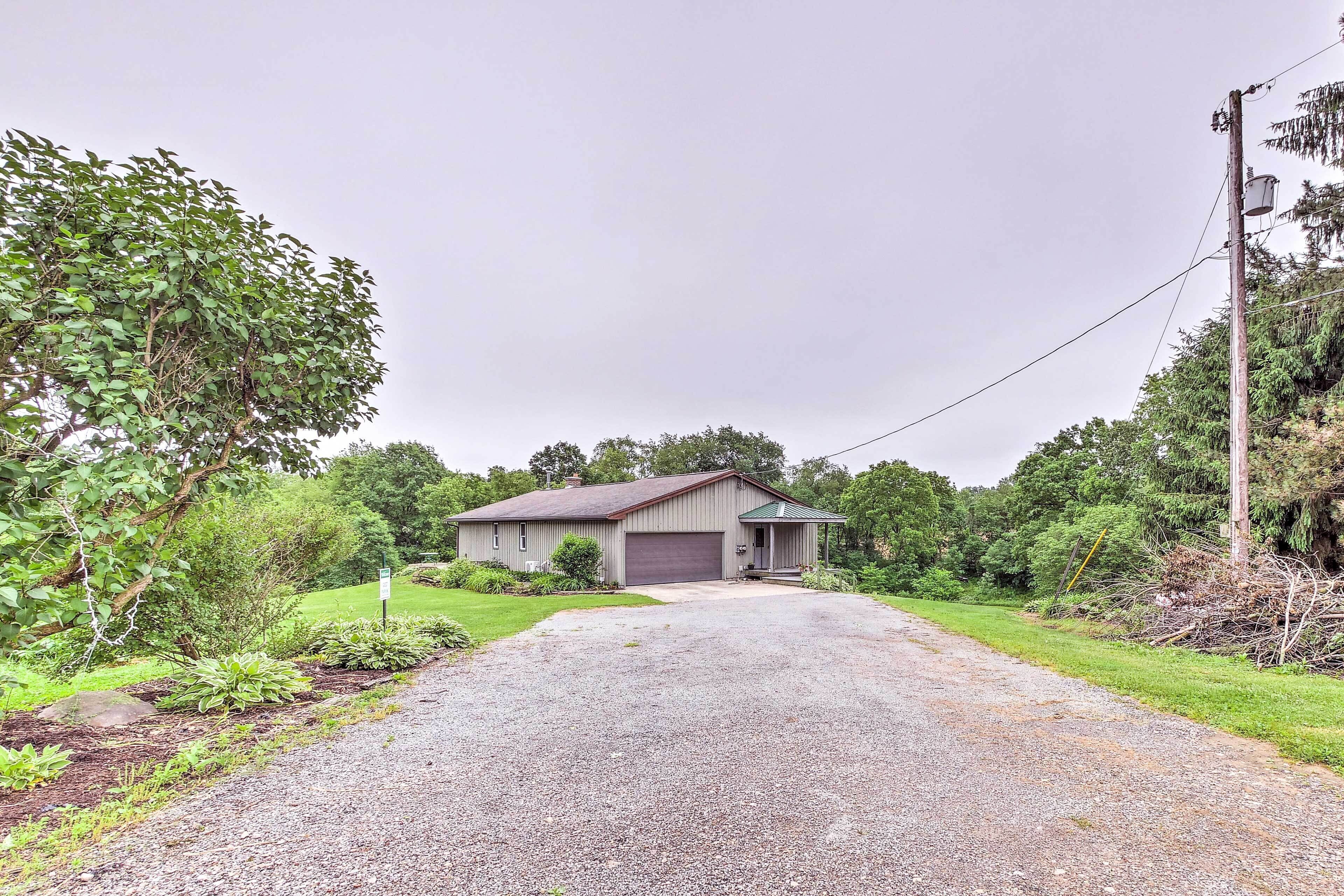 A single-story house with a garage, surrounded by a gravel driveway and lush greenery.