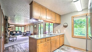 A spacious kitchen with wooden cabinets and a large island, a stone accent wall, and a view of the outdoors through large windows. - 'mimis Place' ~ Ohio Countryside Duplex w/ Deck (Dalton)