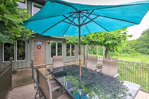 Een tafel met glazen blad en stoelen onder een blauwe parasol, een houten terras en uitzicht op een weelderige tuin.