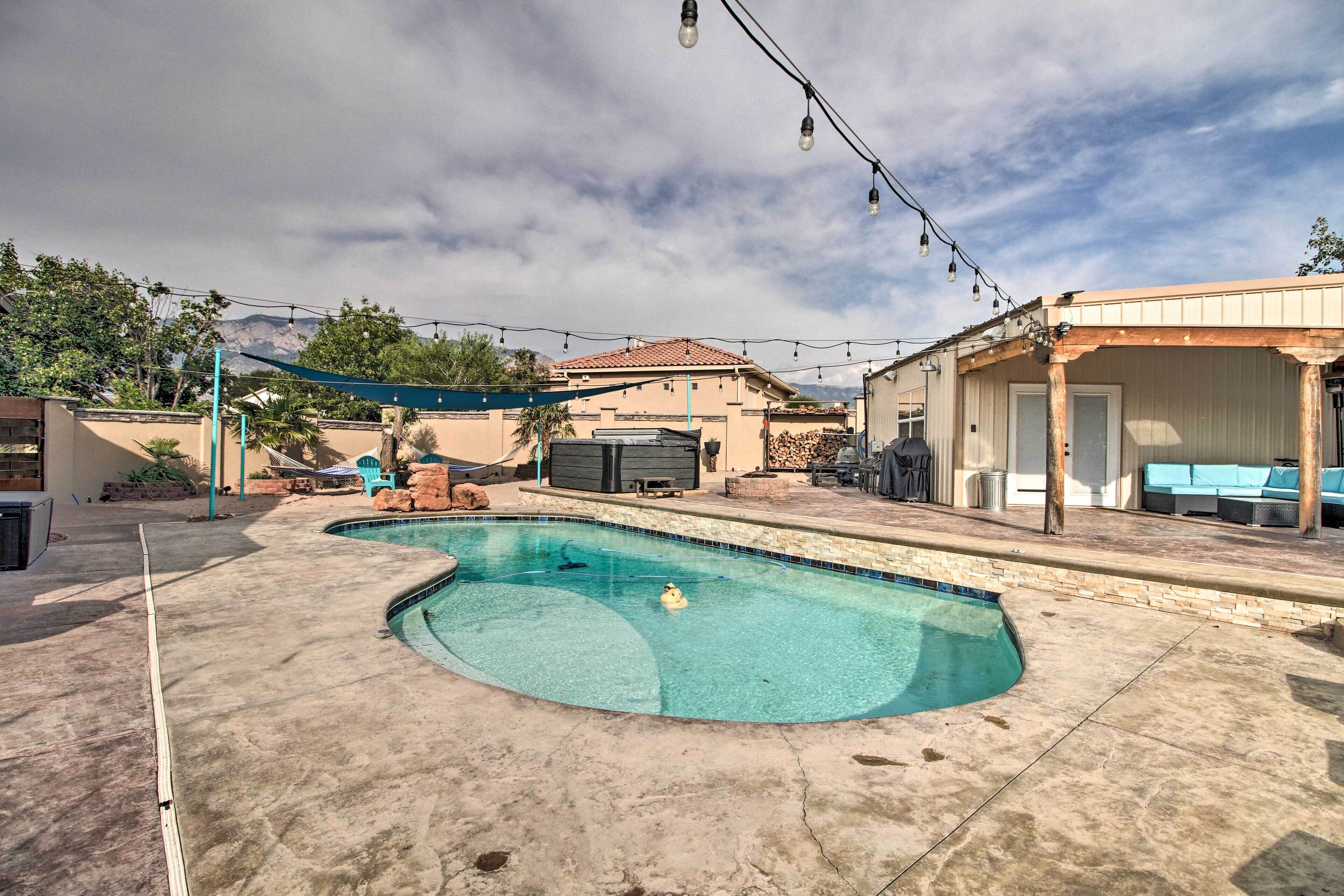A swimming pool with a curved design, surrounded by a concrete deck and a covered patio area with outdoor furniture.
