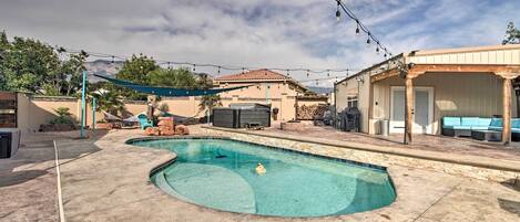 A swimming pool with a curved design, surrounded by a concrete deck and a covered patio area with outdoor furniture.