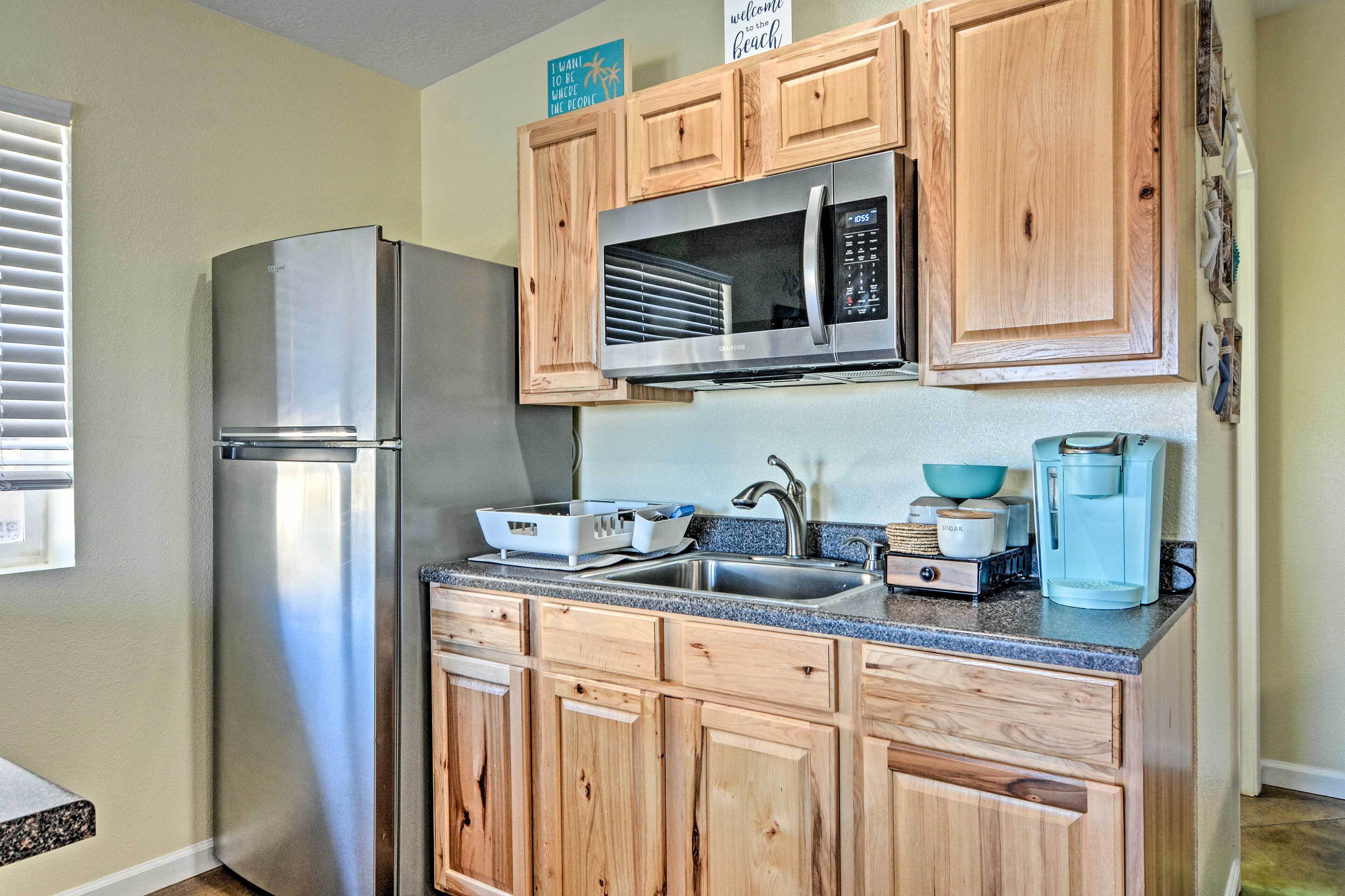 A compact kitchen with wooden cabinets, a stainless steel refrigerator, a microwave, a coffee maker, and a sink.