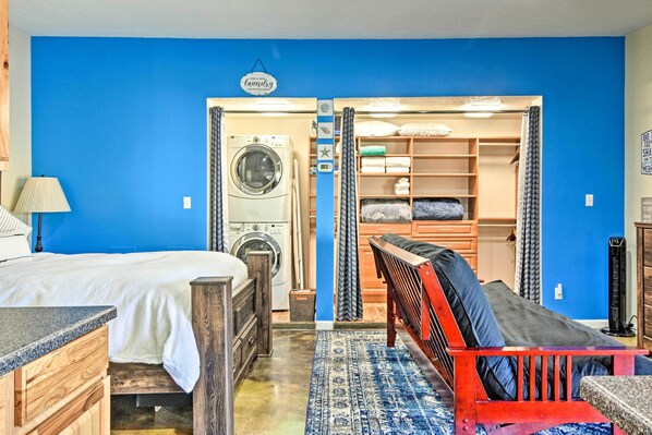 A bedroom with a bed, a washing machine, a closet, and a red chair. - Albuquerque Studio With Shared Pool & Fire Pit! (Albuquerque)