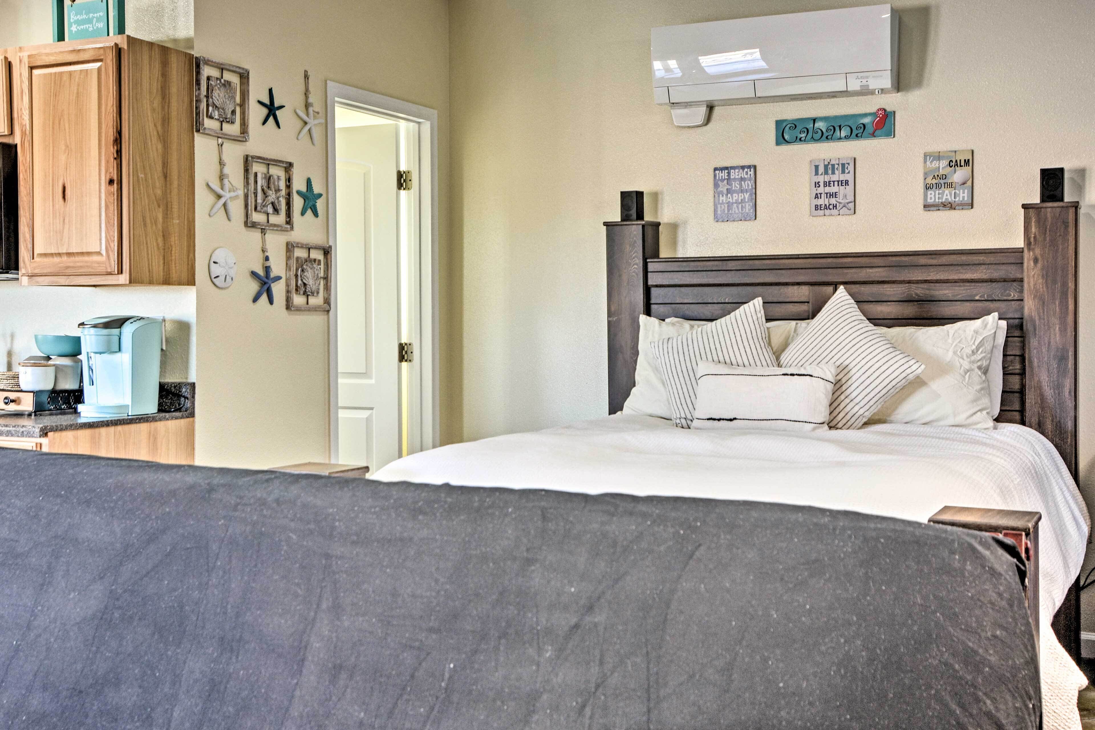 Un dormitorio con cama, cabecera de madera, aire acondicionado de pared y varios objetos decorativos, incluyendo estrellas de mar y un letrero que dice 'Cabana'.