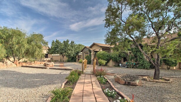 A pathway leading to a building with a covered patio area, surrounded by landscaped gardens and trees. - Albuquerque Studio With Shared Pool & Fire Pit! (Albuquerque)