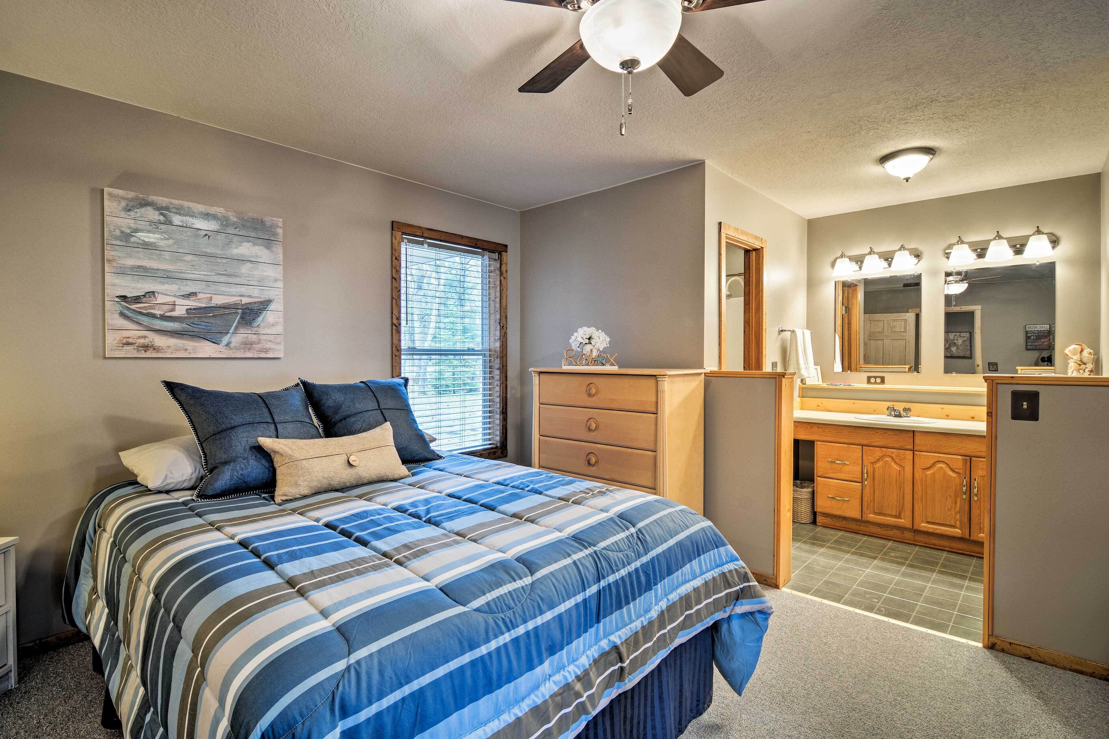 A bedroom with a bed, a dresser, a vanity with a mirror, and a ceiling fan.