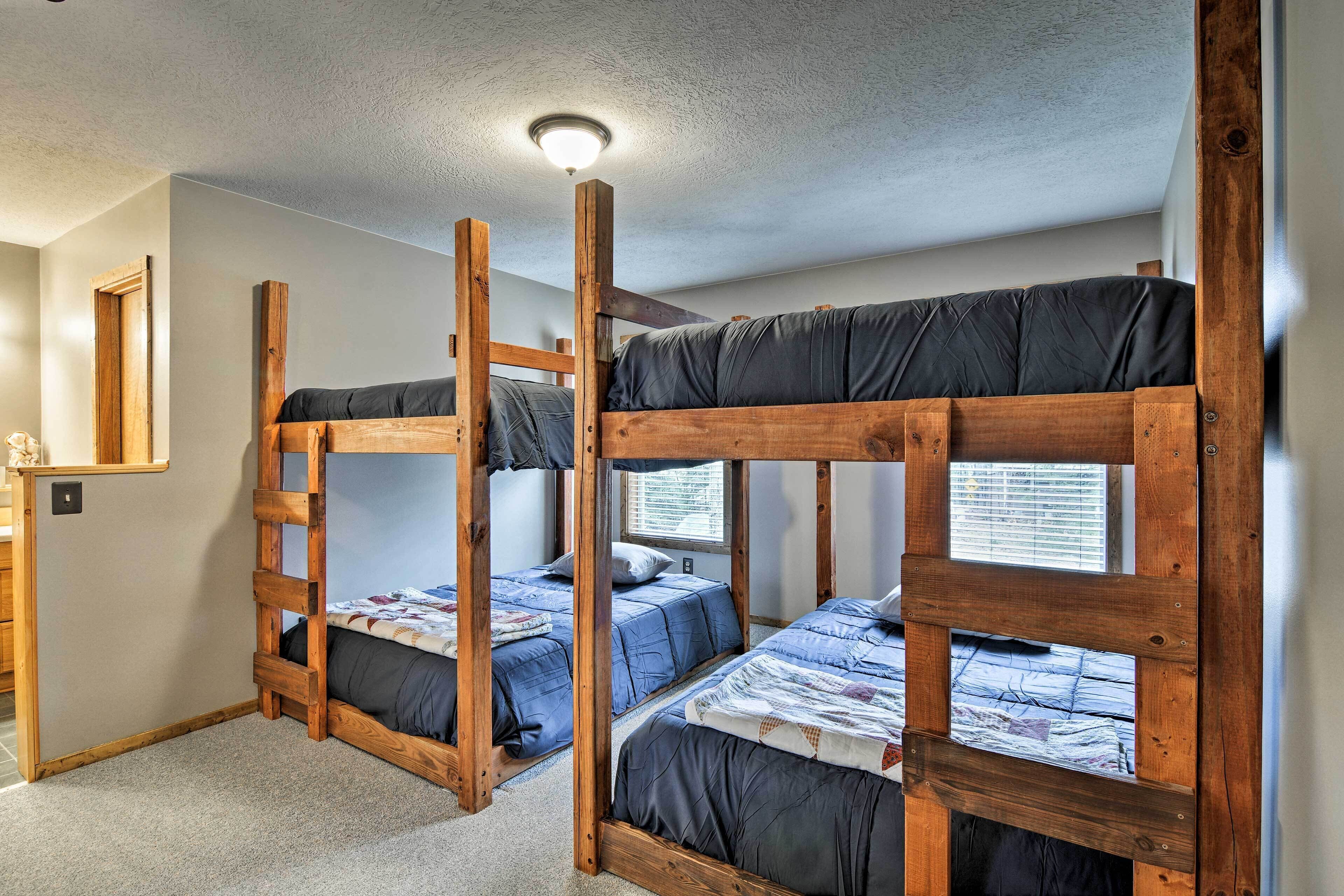A dormitory room with bunk beds, a ceiling light, a window with blinds, and a small desk with a mirror.