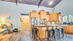 Une cuisine spacieuse avec des meubles en bois, un grand îlot central doté de tabourets, un réfrigérateur et une fenêtre donnant sur un paysage verdoyant.