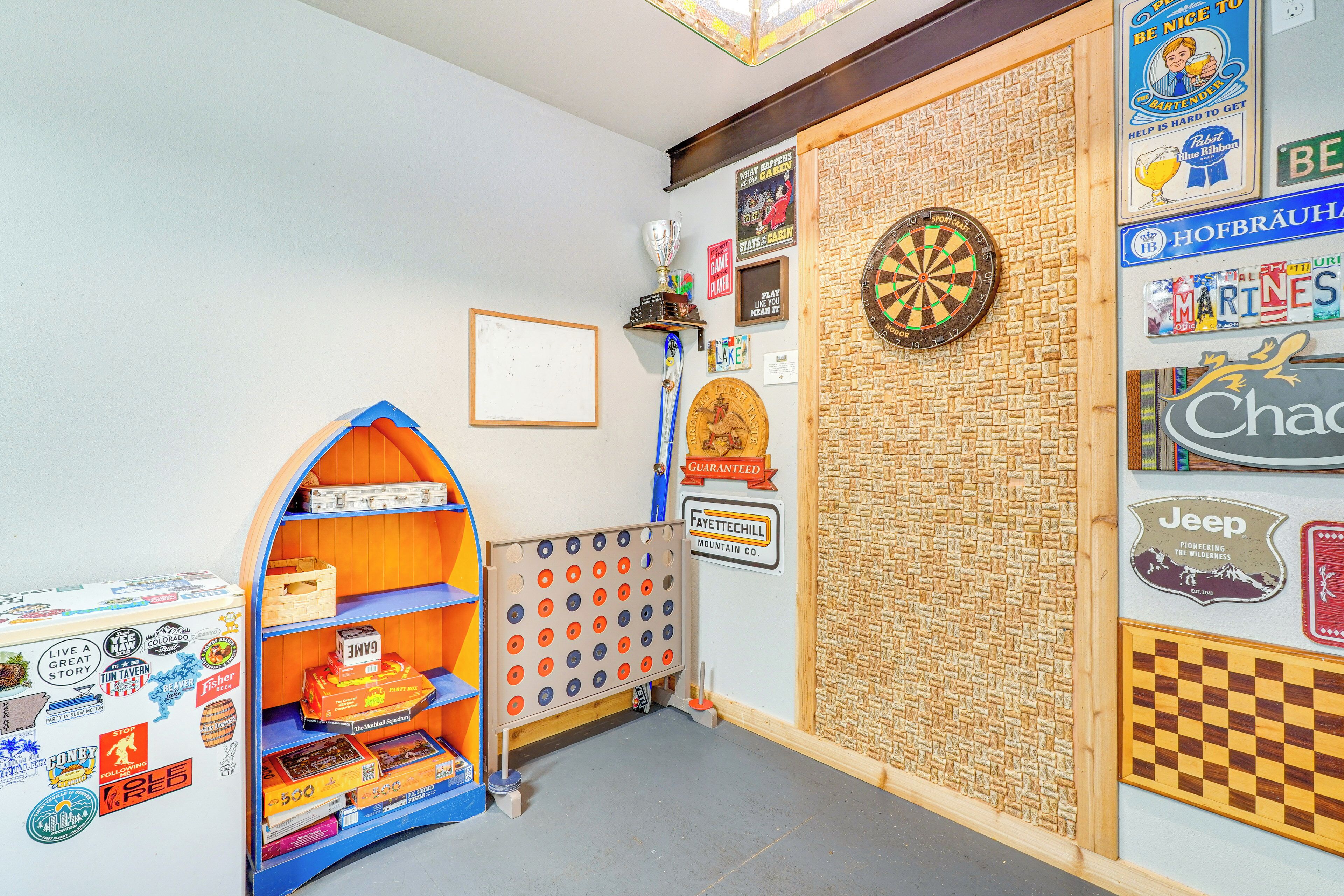 A room with a dartboard, a shelf with board games, and various wall decorations including a Jeep sign and a mountain logo.