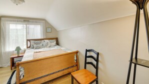A bedroom with a wooden bed, a chair, a bedside table, a floor lamp, and a window with sheer curtains. - Beech Grove Vacation Rental w/ Private Yard (Beech Grove)