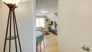 A room with a dining table, chairs, a floor lamp, and a view into another room with a window and plants. - Beech Grove Vacation Rental w/ Private Yard (Beech Grove)