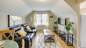 A cozy living room with a black leather sofa, a wooden coffee table, and a TV mounted on the wall. - Beech Grove Vacation Rental w/ Private Yard (Beech Grove)