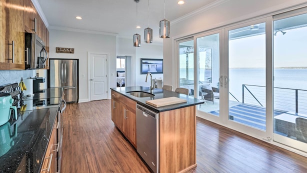 A modern kitchen with a central island, stainless steel appliances, and a large sliding glass door leading to a balcony with a view of the water. - Beautiful Waterfront Getaway w/ Dock! (Abbeville)