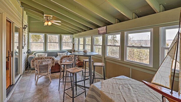 A spacious room with a high ceiling, large windows, a dining area with chairs and a table, and a sailboat model. - Auburn Vacation Rental Home Near Owasco Lake! (Auburn)