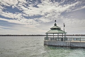 A gazebo with a metal roof and a lantern post on a stone pier extending into a body of water.
