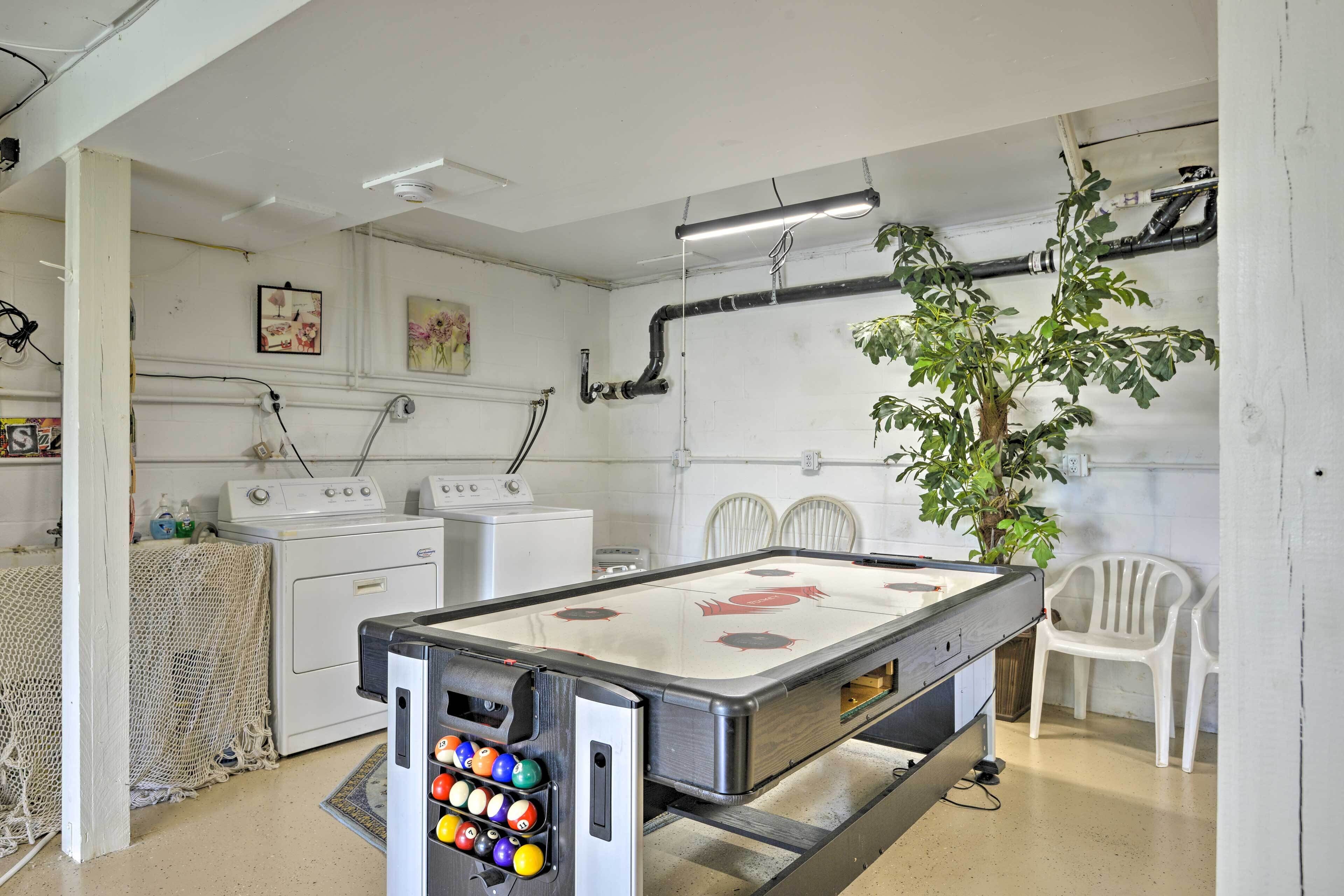 A pool table with a pool ball rack, a washing machine, a dryer, and a plant in a room with white walls and a ceiling fan.
