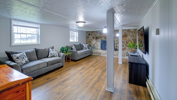 A spacious living room with hardwood flooring, a grey sofa set, a wooden coffee table, and a stone accent wall. - Bluefield Home w/ Covered Deck - Near Parks! (Bluefield)