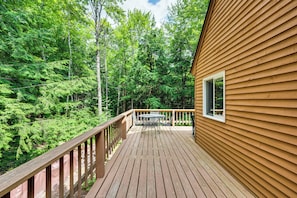 A wooden deck with a table and chairs, surrounded by dense forest. - Bartlett Vacation Rental w/ Wraparound Deck! (Bartlett)