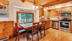 A wooden interior with a dining table, chairs, a kitchen with stainless steel appliances, and a window with a view of greenery. - Bartlett Vacation Rental w/ Wraparound Deck! (Bartlett)