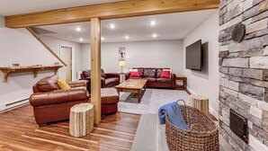 A modern living room with a stone wall, leather sofas, wooden beams, and a flat-screen TV. - Bartlett Vacation Rental w/ Wraparound Deck! (Bartlett)