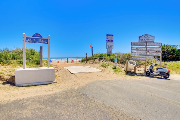 Un panneau indiquant l’accès à la plage, un scooter et un chemin menant à la plage.