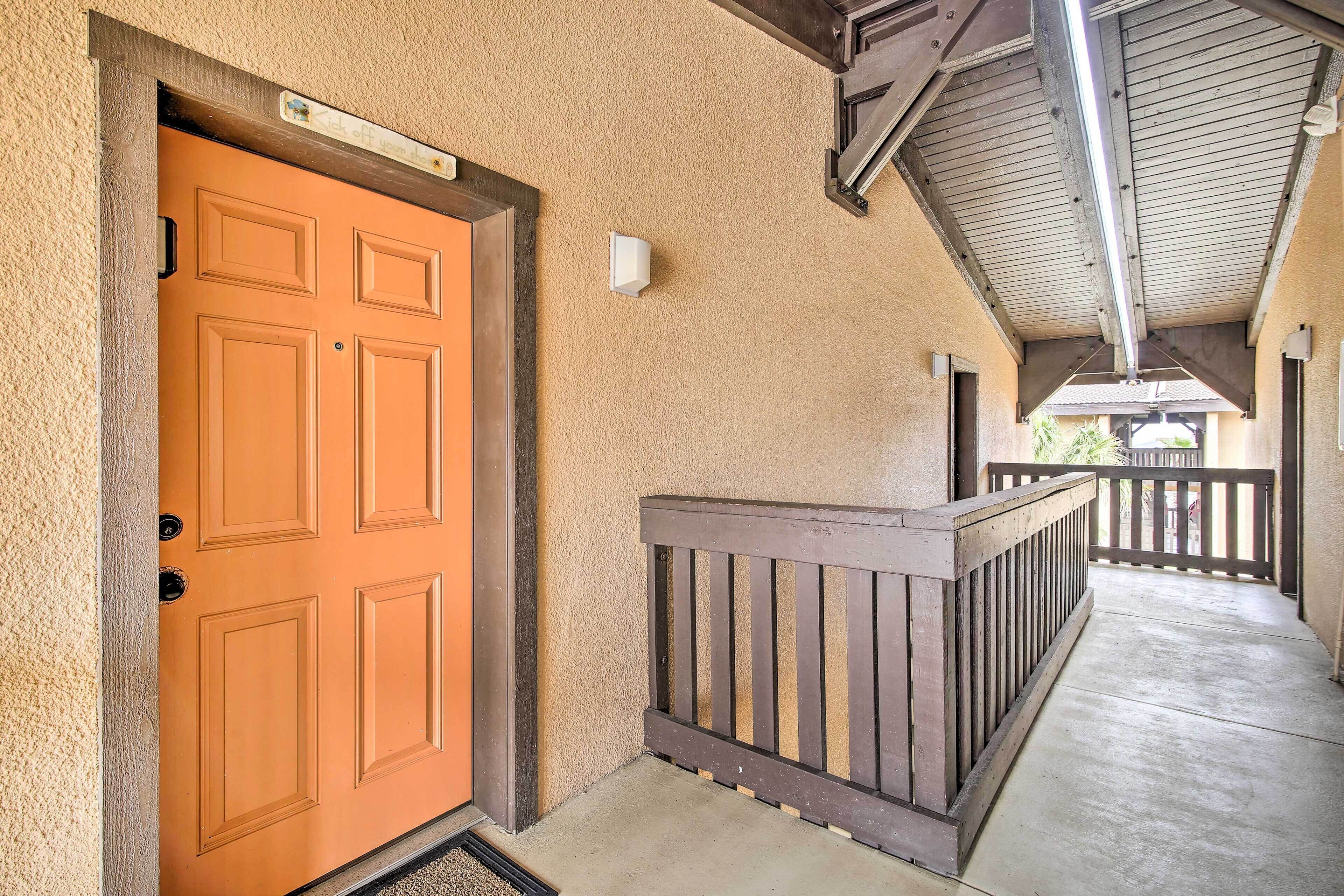 A corridor with a wooden bench, a beige textured wall, and an orange door.