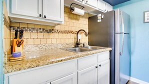 A kitchen with white cabinets, a granite countertop, a stainless steel refrigerator, and a tiled backsplash.