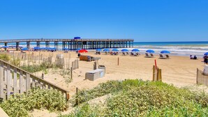 A beach with a wooden pier, beach umbrellas, and lounge chairs.
