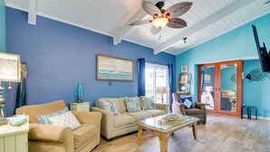 A living room with a blue wall, wooden flooring, a ceiling fan, and a glass coffee table.