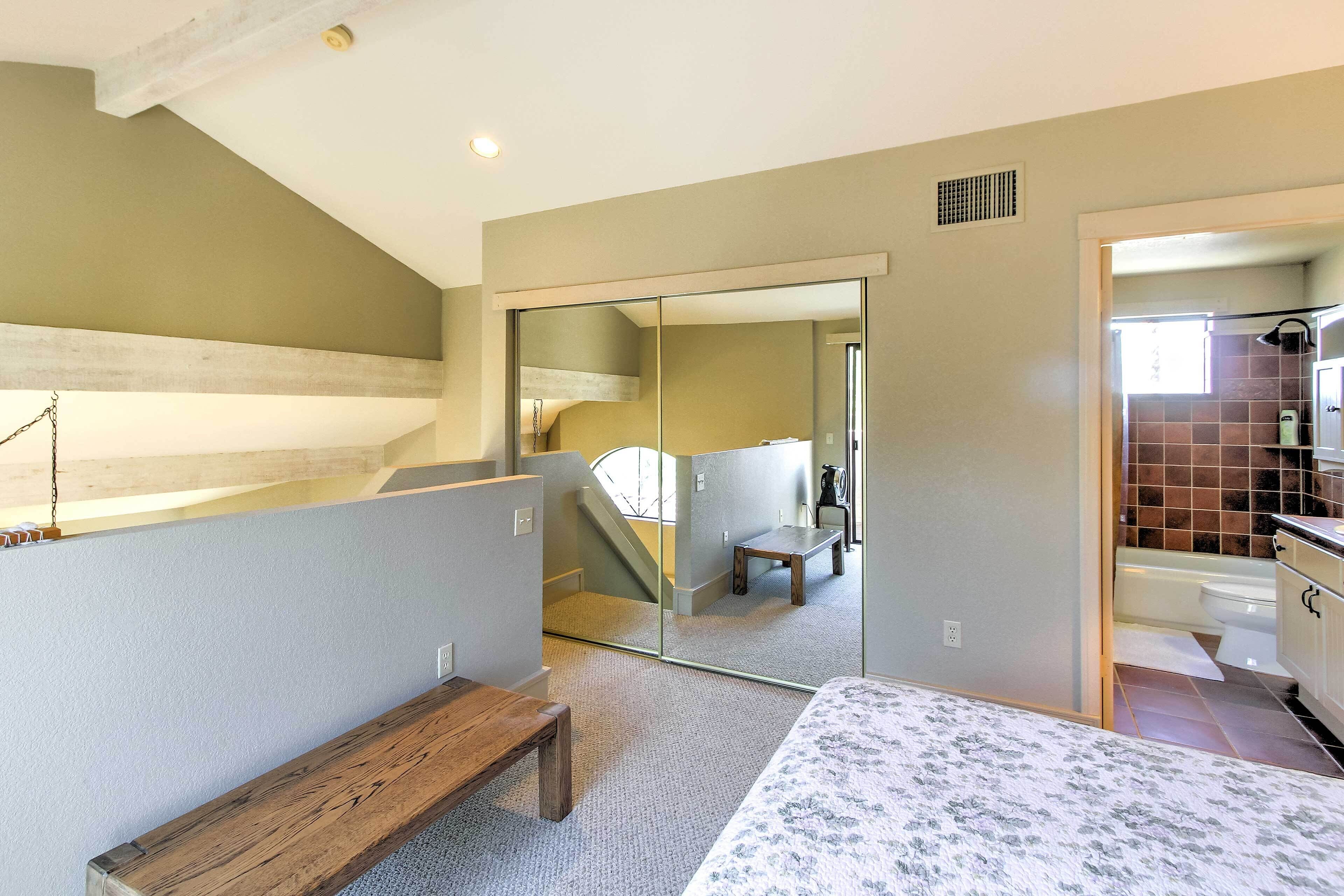 A bedroom with a bed, a bench, a mirror, and a view of a bathroom.