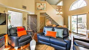 A modern living room with a black leather sofa, a white vase with branches, and a large window with a view of the street. - Borrego Springs Condo w/ Private Hot Tub & Views! (Borrego Springs)