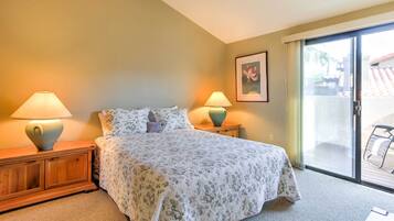 A bedroom with a bed, two bedside tables with lamps, a framed picture on the wall, and a sliding glass door leading to an outdoor area.