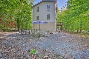 Ein zweigeschossiges Gebäude mit einer Terrasse, die mit einem Tisch und Stühlen möbliert ist und von Bäumen umgeben wird.