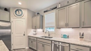 A modern kitchen with grey cabinets, stainless steel appliances, a white door, and a clock on the wall. - Beaufort Townhome w/ Game Room: 8 Mi to Beaches! (Beaufort)