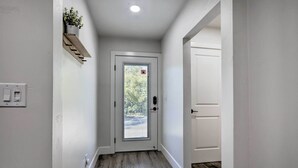 A narrow hallway with a white door, a small plant on a shelf, and a light switch on the wall.